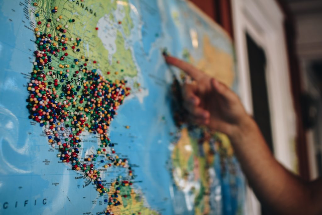 Person pointing to a place on the map which has pins all over it