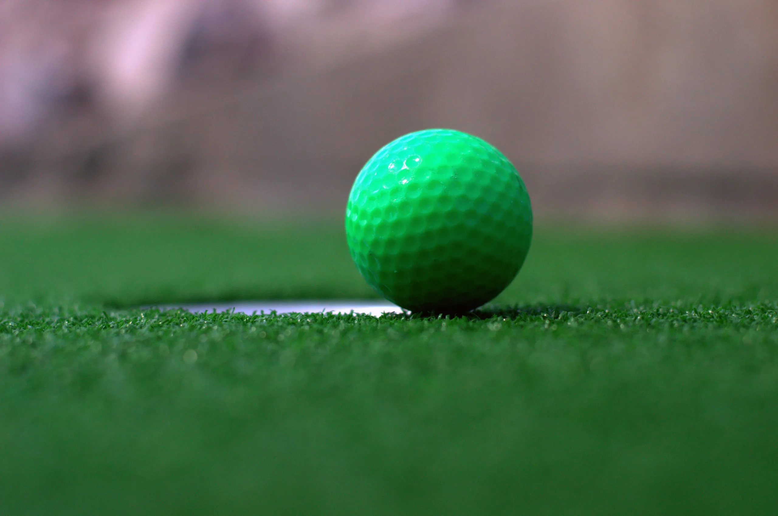 Green mini-golf ball by a hole